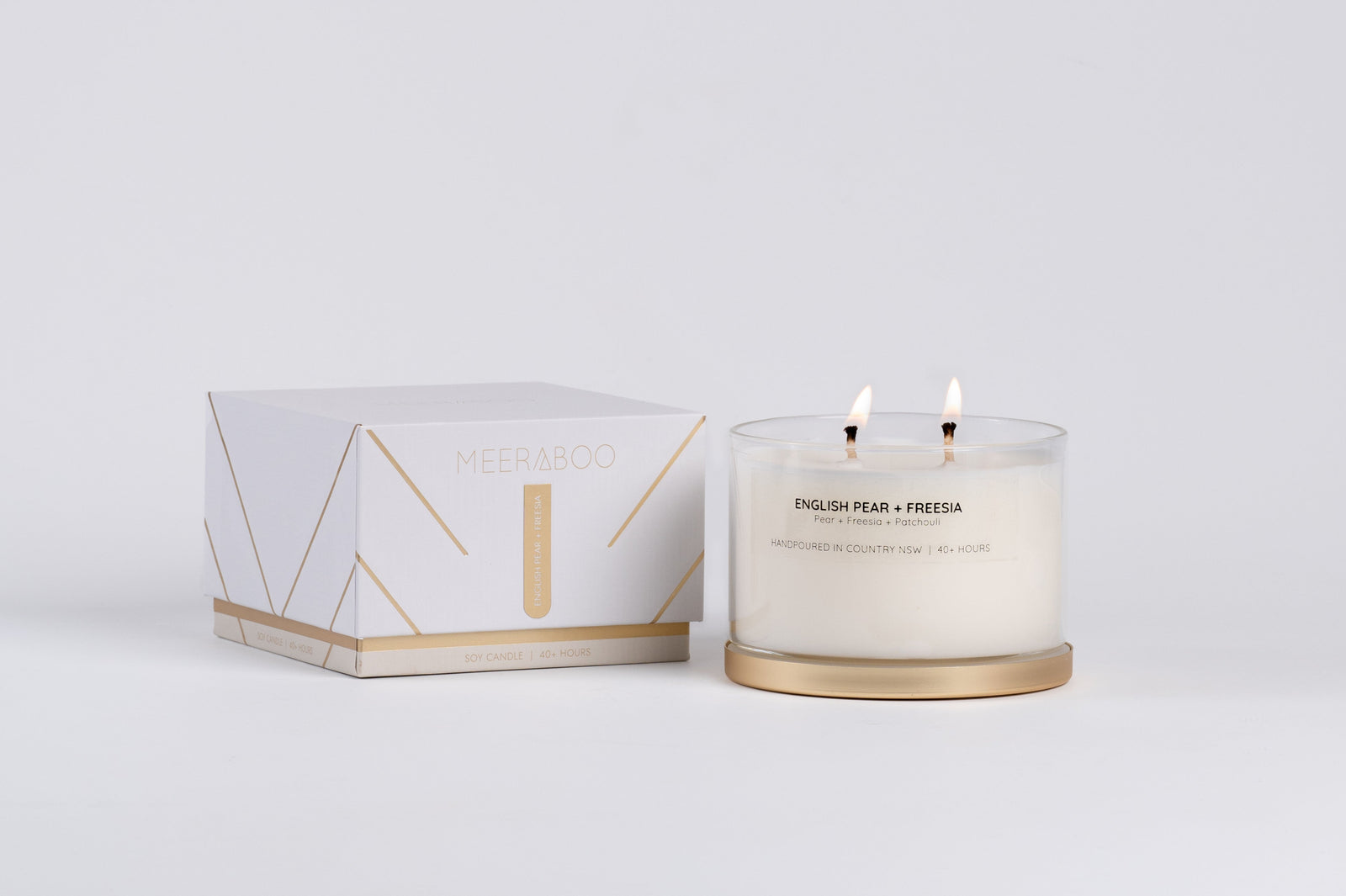 Four lit candles with gold bases on a white surface, surrounded by greenery.