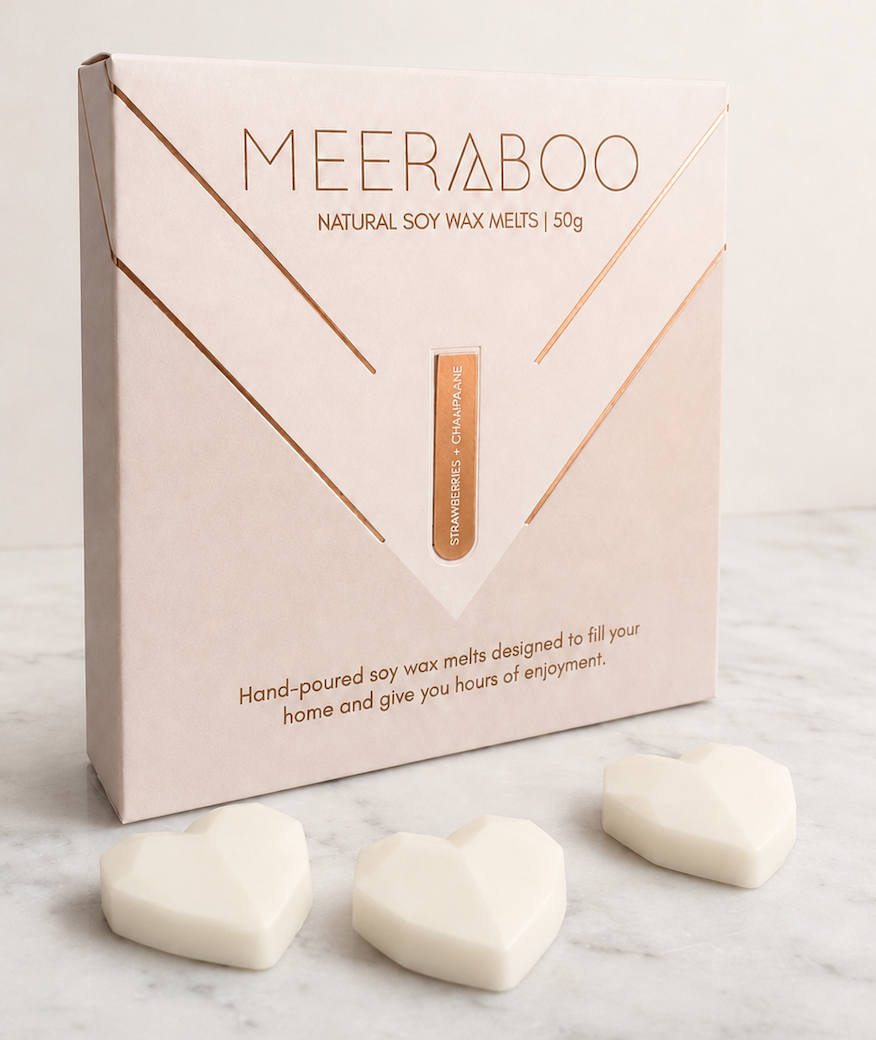 A box of MEERABOO Natural Soy Wax Melts displayed on a white marble surface with three heart-shaped white wax melts in front.