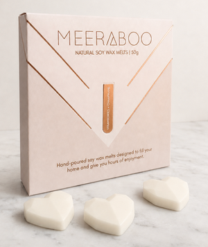 A box of MEERABOO Natural Soy Wax Melts displayed on a white marble surface with three heart-shaped white wax melts in front.